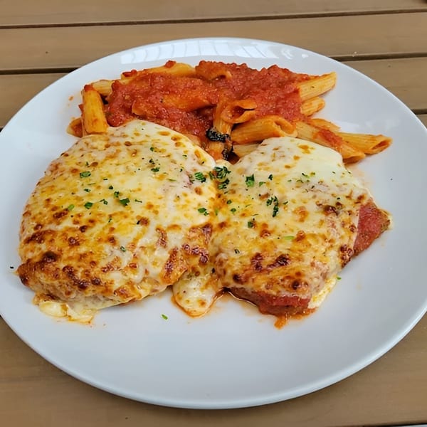 Chicken parmesan with melted cheese and penne pasta in red sauce on a white plate.