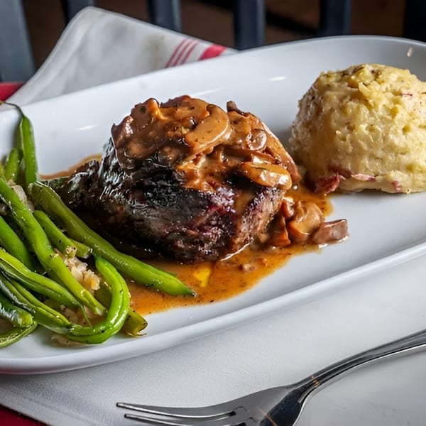 Steak with mushroom sauce, green beans, and mashed potatoes on a white plate.